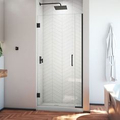 a bathroom with white walls and wood flooring has a glass shower door that is open