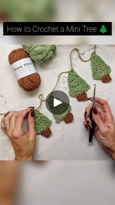 someone is crocheting small christmas trees on a table with yarn and scissors in front of them