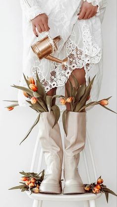 a woman wearing white boots and holding a gold cup with flowers on the bottom, sitting on a stool