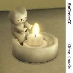 a small white teddy bear sitting next to a lit candle