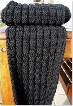 a black knitted scarf hanging from a wooden rail