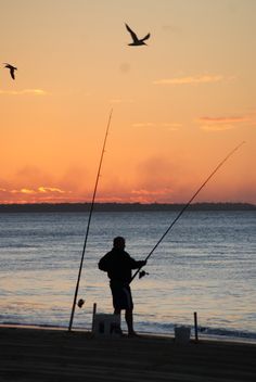 a man fishing on the beach at sunset