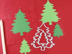 paper cut out of christmas trees on a red surface with a pencil and eraser