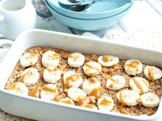 a white dish filled with oatmeal and banana slices on top of a table