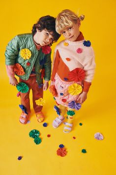 two young children standing next to each other on a yellow background with confetti scattered around them