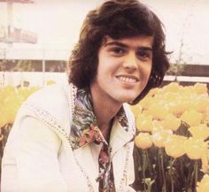 a young man sitting in front of yellow flowers