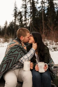 a man and woman kissing while sitting on a bench with two mugs in front of them