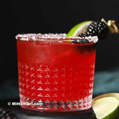 a close up of a red drink with lime and blackberries on the rims