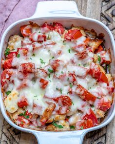 a casserole dish with tomatoes, cheese and meat in it on a wooden table