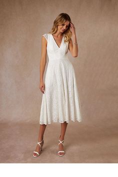 a woman is wearing a white dress and heels with her hand on her head while standing in front of a beige background