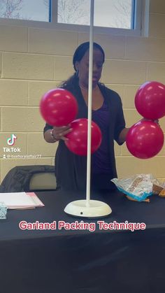 a woman holding red balloons in front of a black table with white poles on it