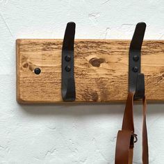 a wooden coat rack with two leather straps hanging from it's hooks on a white wall