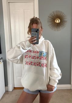 a woman taking a selfie in front of a mirror wearing shorts and a hoodie