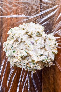 a bowl filled with food sitting on top of a wooden table covered in plastic wrap