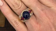 This exquisite ring is centered with an oval, sapphire cabochon in a partial bezel setting. The shoulders are each channel set with four (4) square mixed cut rubies. The top of the ring is bead set with a total of forty-six (46) round brilliant cut diamonds. The ring measures 13.7mm at the top, rises 11.2mm above the finger, tapering to 5.5mm wide and 1.3mm thick at the base of the shank. This ring is currently a size 7. Ruby Diamond Ring, Sapphire Cabochon, Ruby Diamond Rings, Bead Set, Ruby Diamond, Channel Set, Round Brilliant Cut Diamond, Bezel Setting, Round Brilliant