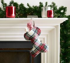 a plaid stocking hanging from a fireplace mantel with candles on the mantle behind it