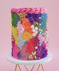 a multicolored cake sitting on top of a white table next to a pink wall