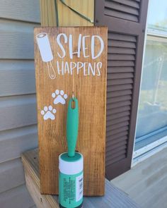 a wooden sign that says shed happens with a green paint roller and dog paw print on it