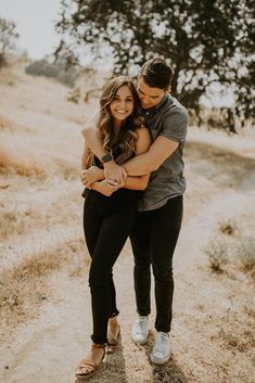 a man and woman hugging each other on a dirt road