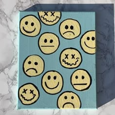 a blue box with yellow smiley faces painted on the front and sides, sitting on a marble surface