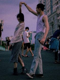 two people are dancing in the street at dusk with other people walking around behind them