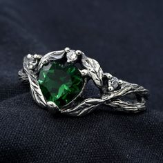 a green heart shaped ring sitting on top of a black cloth with leaves around it