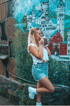 a woman standing in front of a wall with barrels painted on it's side