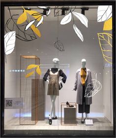 two mannequins in front of a window display with yellow and white leaves