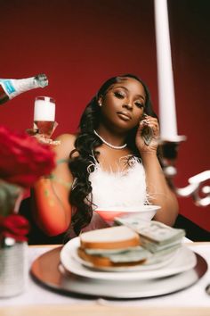 a woman sitting at a table with food and drinks in front of her on the phone