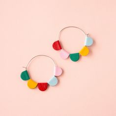 two pairs of hoop earrings with multicolored paper circles on each earring, against a pink background