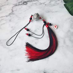 a red and black tasseled necklace on a marble surface