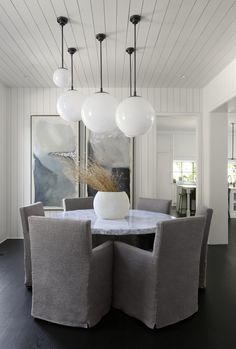 the dining room table is surrounded by gray chairs and white globe lights hanging from the ceiling