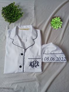 a white shirt with monogrammed initials on it and a green plant next to it