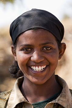 a smiling young woman wearing a black head scarf and a green shirt with brown buttons