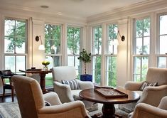 a living room filled with lots of furniture next to two large windows covered in curtains