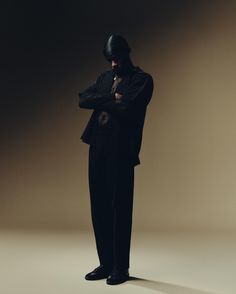 a man in a black suit and hat standing with his arms crossed looking at the camera