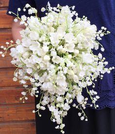 a bouquet of white flowers is held by a woman's arm in front of a wooden wall