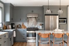 a kitchen with gray cabinets and marble counter tops, stainless steel appliances and wooden chairs