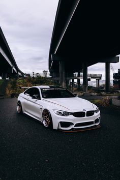 the white car is parked on the side of the road near an overpass with traffic lights