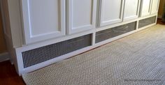 a kitchen with white cabinets and black grates on the floor in front of it