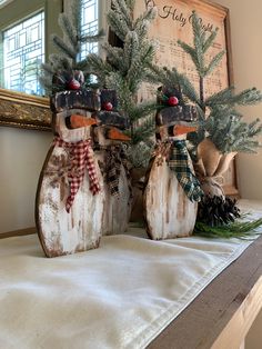 two wooden snowmen sitting on top of a table next to pine cones and evergreen branches