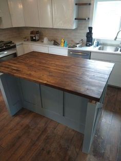 a kitchen with an island in the middle and white cabinets on both sides, along with wooden flooring