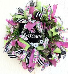 a welcome wreath with pink, green and black ribbons on the front door for someone's house