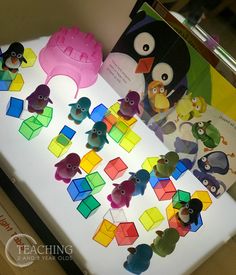 there are many different colored toys on the table with an open book about penguins and cubes