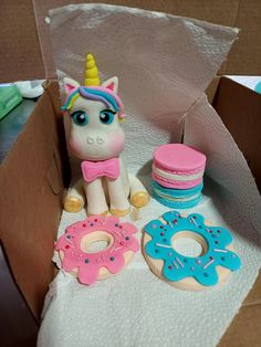 there is a toy unicorn sitting next to doughnuts and donuts in a box