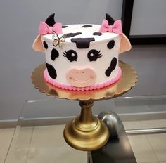 a cake decorated with a cow face and pink bow on top of a gold plate