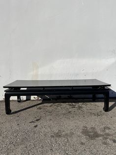 a black coffee table sitting on top of a cement floor next to a white wall