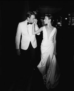 a black and white photo of a man and woman in formal wear, walking together