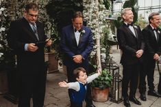 a little boy standing in front of a group of men wearing tuxedos and bow ties