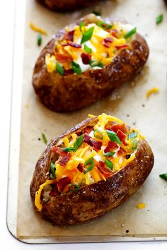 three baked potatoes with cheese and green onions on a baking sheet, ready to be eaten